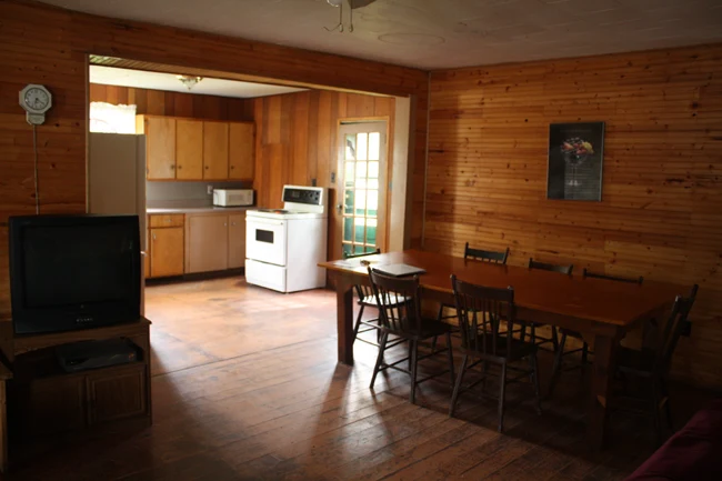 Pigeon Lake Resort Cottage Two.&nbsp; Dining area with table and chairs connected to a kitchen in a wood-paneled cottage interior.